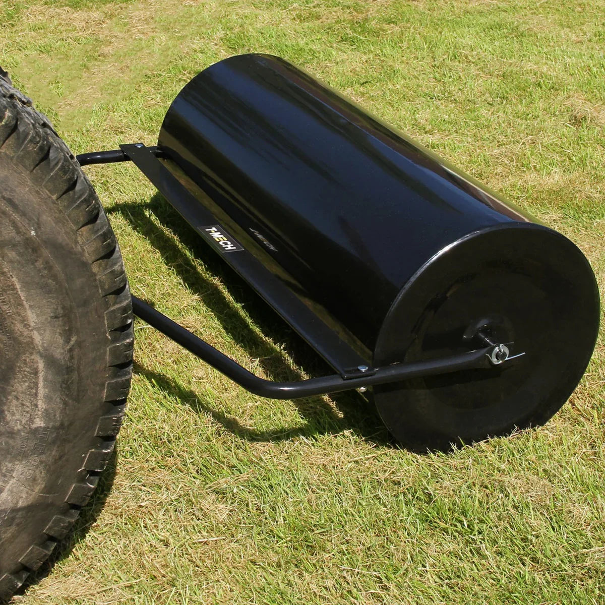 T-Mech 120L towable garden roller with a sleek black metal drum, sturdy frame, and textured surface, set on green grass