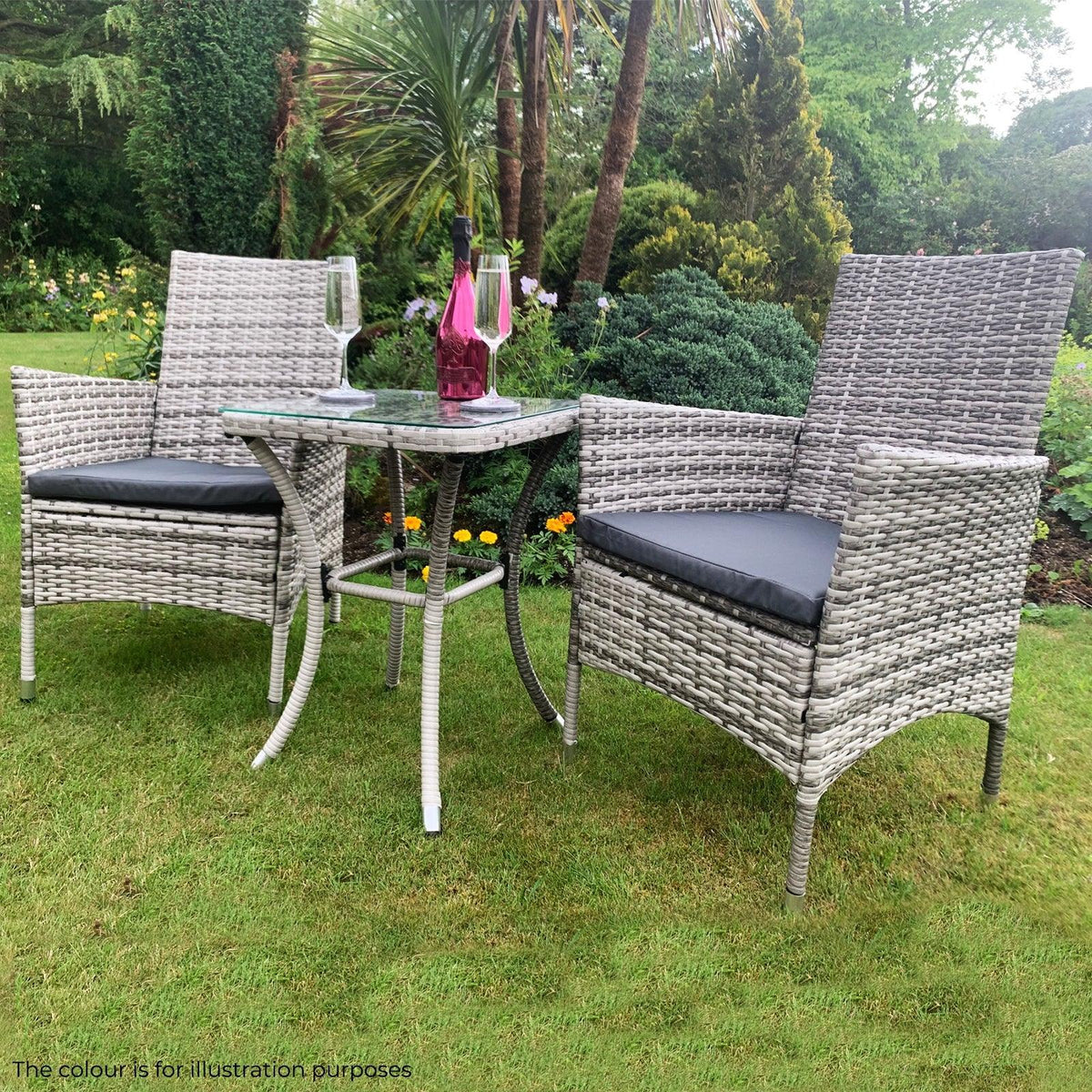 Light grey rattan bistro set featuring two chairs with cushions and a matching table, set in a lush garden with vibrant flowers