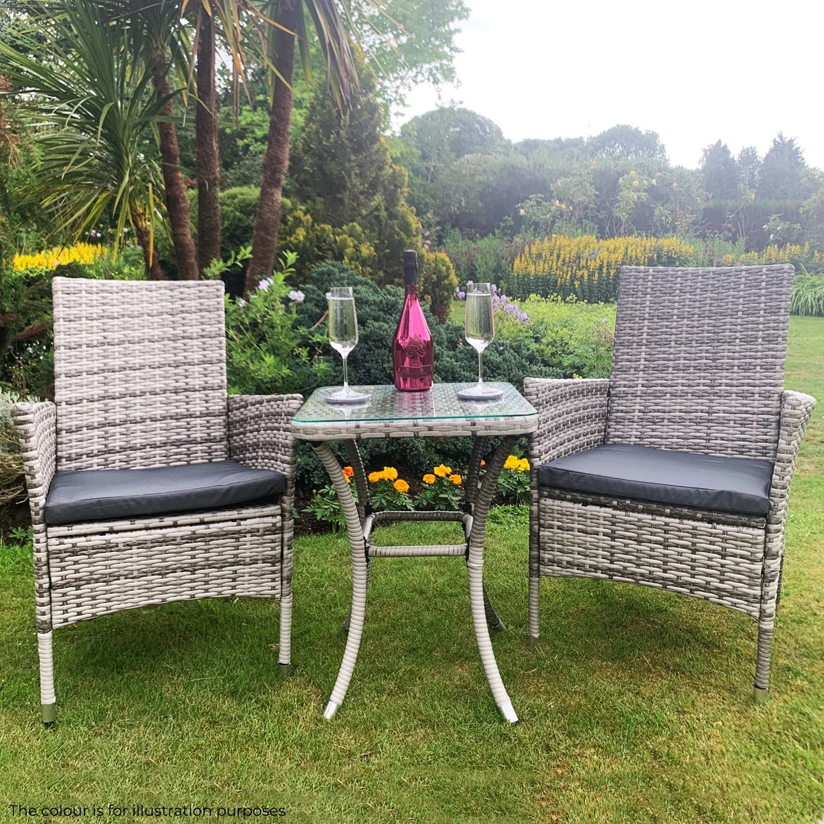 Light grey rattan bistro set featuring two chairs with cushions and a glass-top table, set in a lush garden with flowers