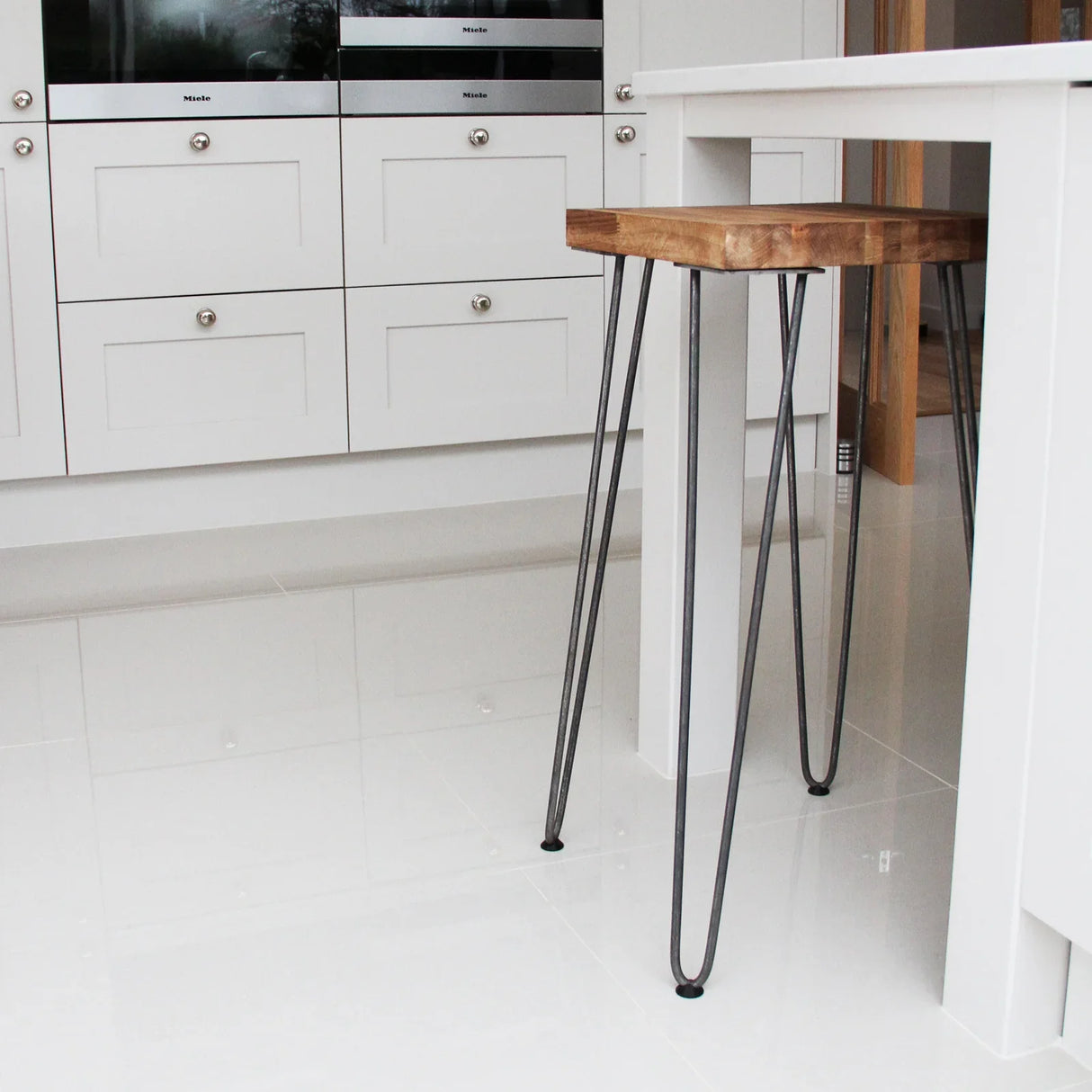 Black 12mm hairpin legs with three prongs, showcasing a sleek design, supporting a wooden tabletop in a modern kitchen setting