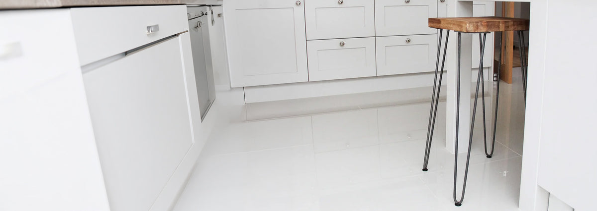Modern kitchen featuring sleek white cabinetry, glossy floor tiles, and a rustic wooden stool with metal legs for a stylish contrast