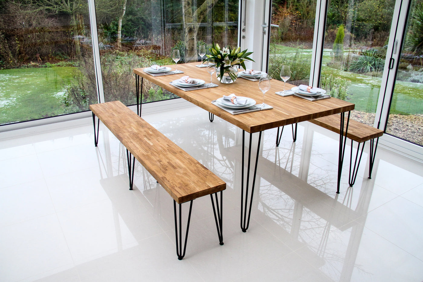 Modern wooden dining table with a natural finish, supported by sleek black metal legs, accompanied by matching benches and elegant table settings