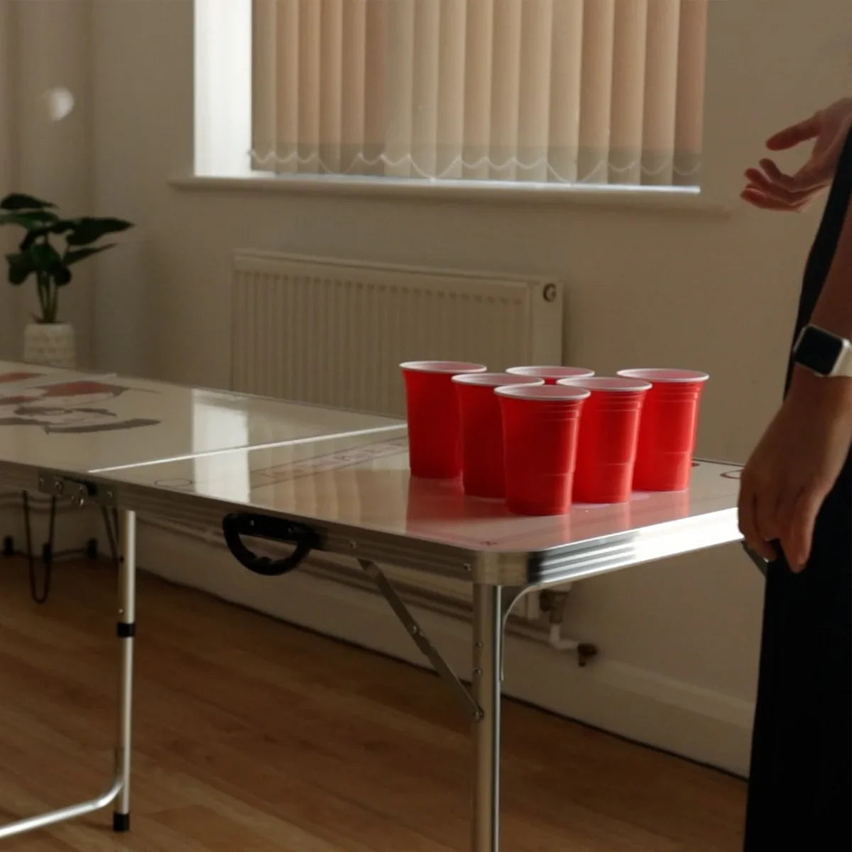8FT beer pong table with a glossy surface, featuring six red plastic cups arranged for gameplay, set in a bright indoor space