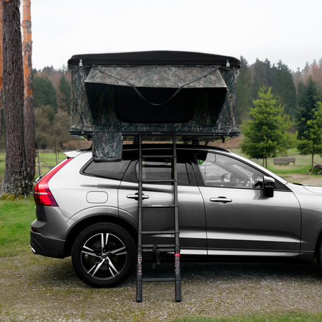 A rugged car roof tent in camouflage, elevated on a silver SUV, with a sturdy ladder leading up to the entrance, surrounded by greenery
