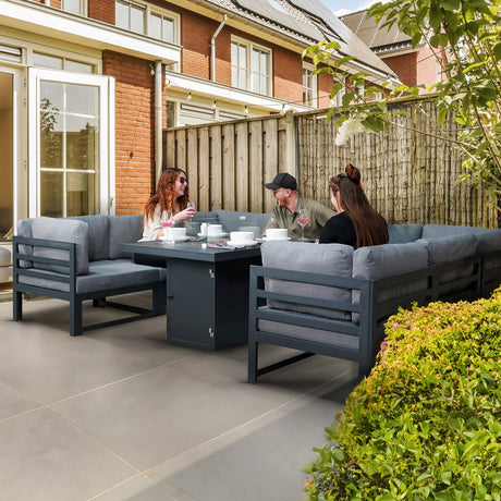 Stylish outdoor dining set with gray cushions, a sleek black table, and three friends enjoying a meal in a cozy garden setting