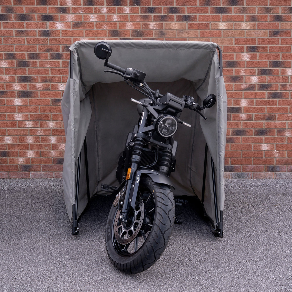 Compact motorbike tent in gray, featuring waterproof material and sturdy frame, securely housing a sleek black motorcycle against a brick wall
