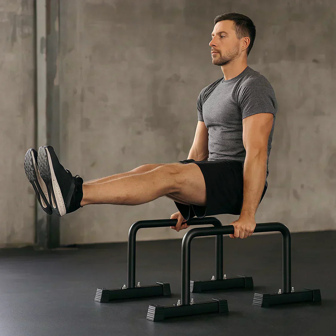 A fit man performs a leg raise on black parallel bars, showcasing strength and balance in a modern, minimalistic gym space