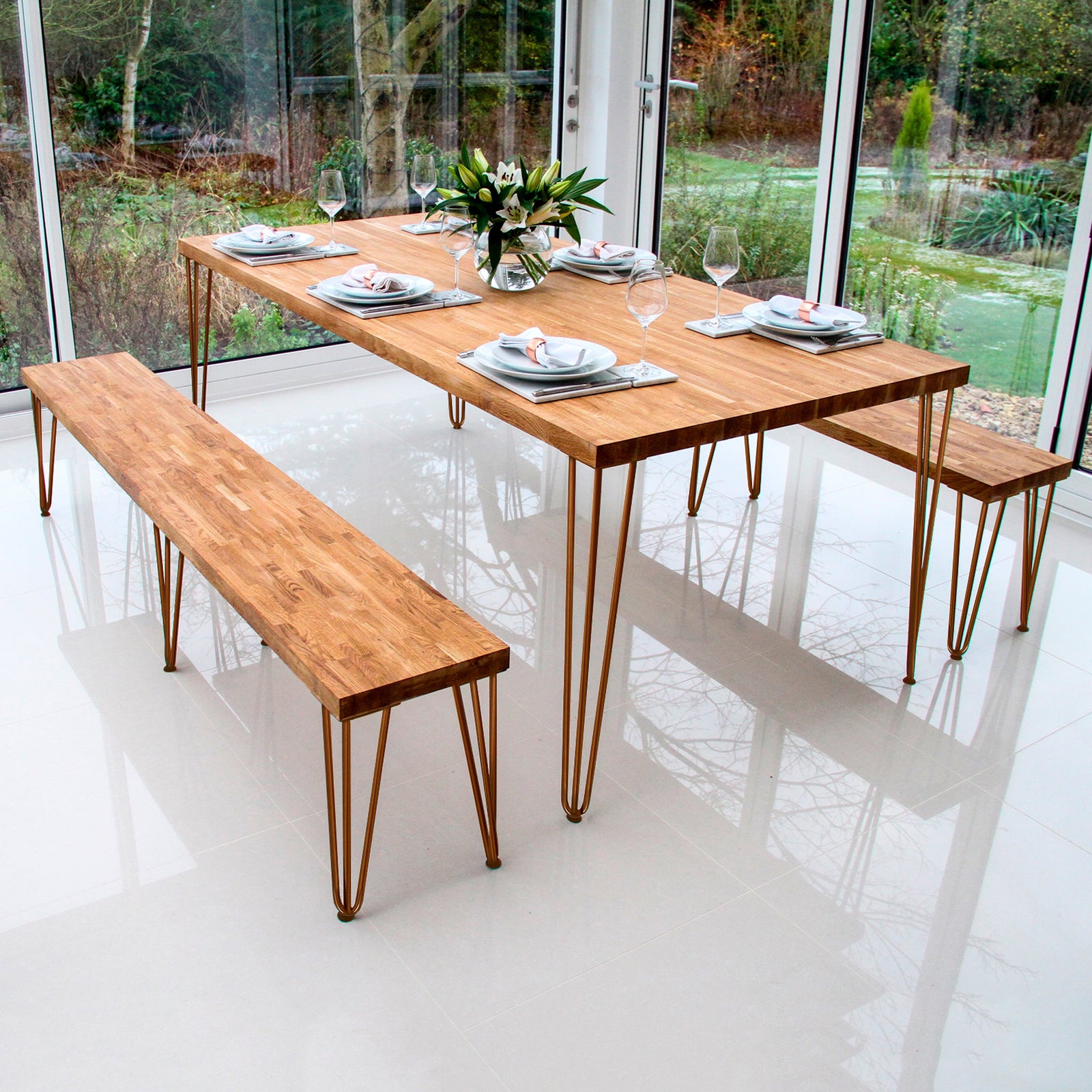 Stylish wooden dining table with metal legs, set with plates and glasses, surrounded by a bright, modern glass-walled space