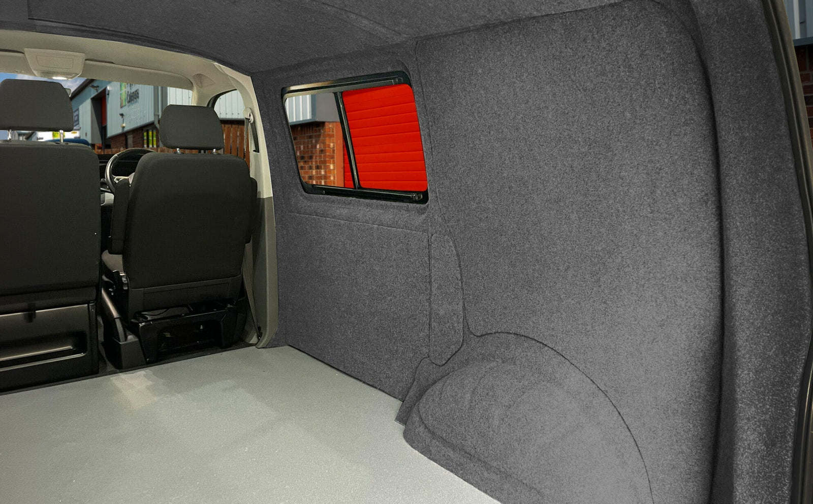 Interior of a campervan featuring dark gray felt lining, plush texture, and a spacious layout with two black seats visible