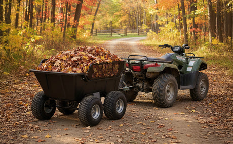 A rugged ATV towing a black trailer filled with colorful autumn leaves on a dirt path surrounded by vibrant fall foliage