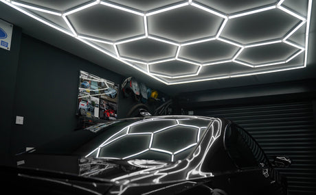 Bright hexagon LED lights illuminate a modern garage ceiling, reflecting off a sleek black car, enhancing the contemporary design