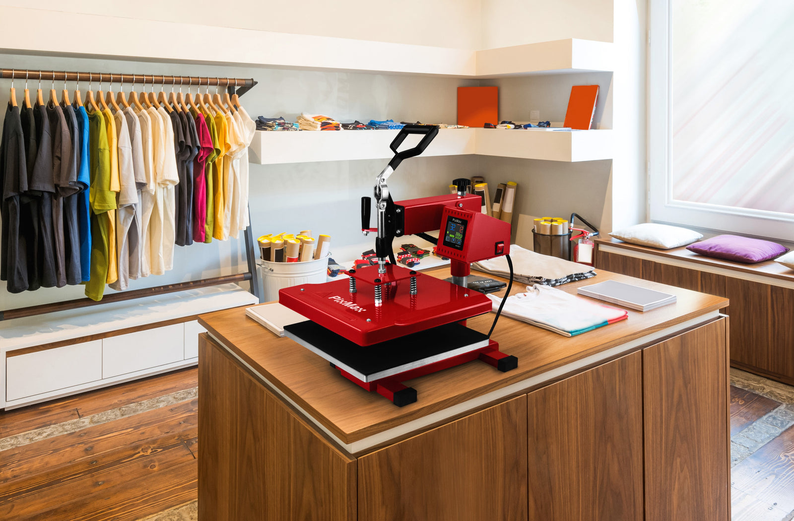A vibrant red heat press machine on a wooden table, surrounded by colorful t-shirts and crafting supplies in a bright workspace