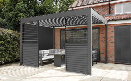 Modern gray pergola with slatted roof, surrounding a cozy outdoor seating area on a stone patio, framed by lush greenery