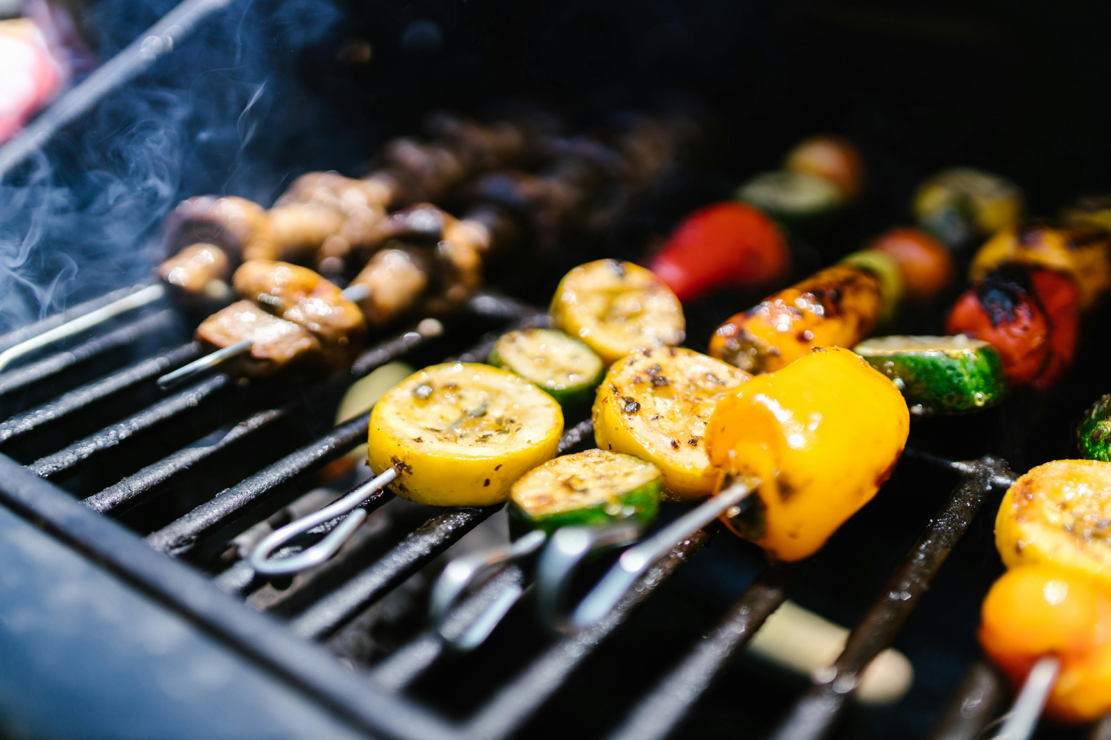Colorful skewers of grilled vegetables and mushrooms sizzling on a portable charcoal BBQ, with smoke rising in the background