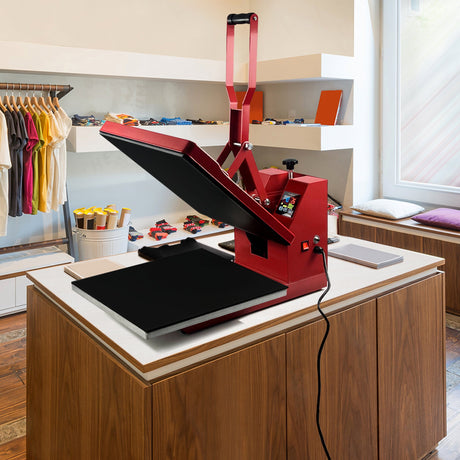 Red heat press machine with a large black platen, positioned on a wooden table in a bright, modern retail space with colorful apparel in the background