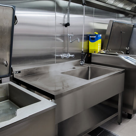 Stainless steel catering sink with a sleek, polished surface, featuring a faucet and adjacent equipment in a commercial kitchen setting