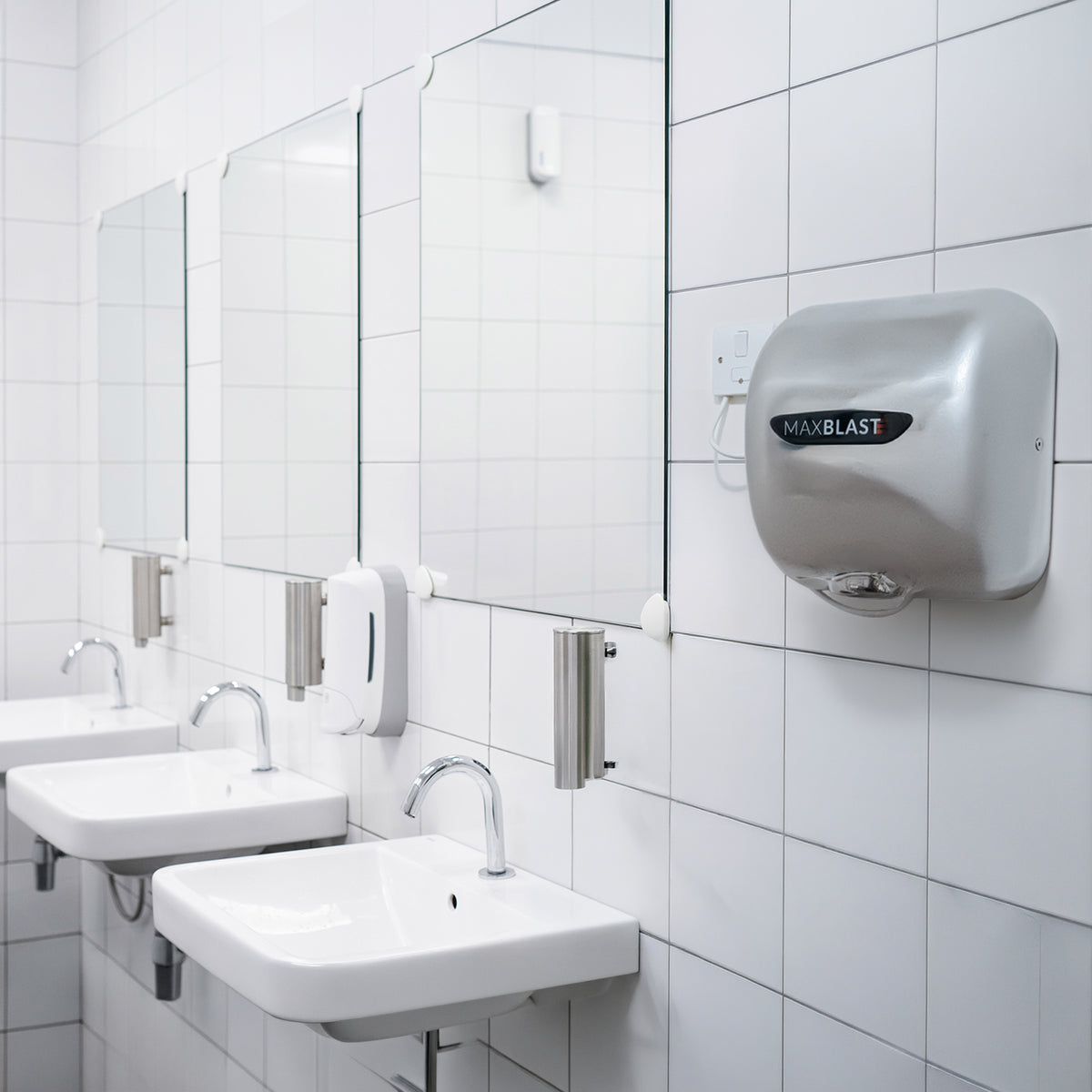 Sleek silver Maxblast automatic hand dryer mounted on a tiled bathroom wall, featuring a HEPA filter and modern design elements