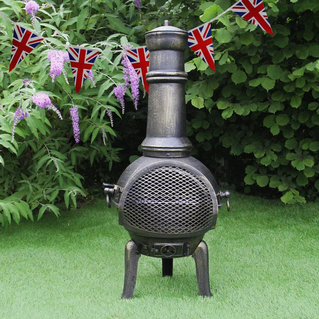 Cast iron chimenea with a tall chimney, mesh front, and Union Jack bunting, set against lush green foliage and grass