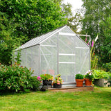 Clear polycarbonate greenhouse with a metal frame, surrounded by vibrant flowers and greenery, ideal for gardening enthusiasts