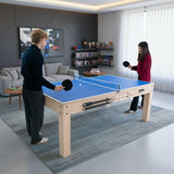 Blue tabletop 7-in-1 games table with two players enjoying table tennis, surrounded by a cozy living room setting with storage benches