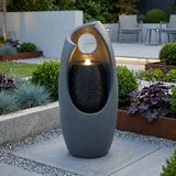 Sleek gray electric water feature with a modern design, featuring cascading water and a soft glowing light, surrounded by lush greenery