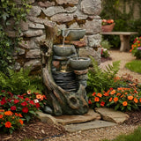 Rustic electric water feature with three stacked bowls cascading water, surrounded by vibrant flowers and textured stone wall