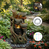Rustic electric water feature with cascading stone bowls, ambient LED lighting, and a natural wood-like finish, surrounded by lush greenery