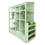 Victorian-style greenhouse in soft green wood, featuring multiple shelves, glass panels, and potted plants for indoor gardening