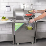 Stainless steel KuKoo sugar cane press with a hand inserting sugar cane, juice flowing into a measuring jug on a countertop