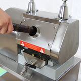 Stainless steel KuKoo sugar cane press with a hand inserting a sugar cane stalk into the feed opening, featuring safety warnings