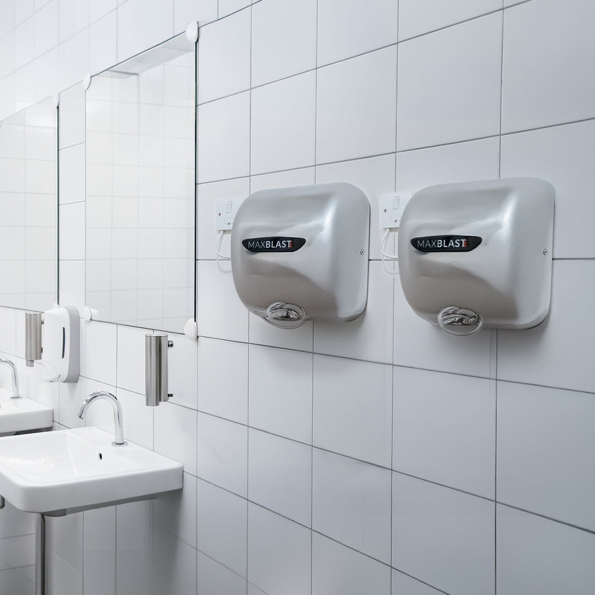 Sleek silver MAXBLAST hand dryers mounted on a tiled bathroom wall, reflecting light and enhancing modern restroom aesthetics