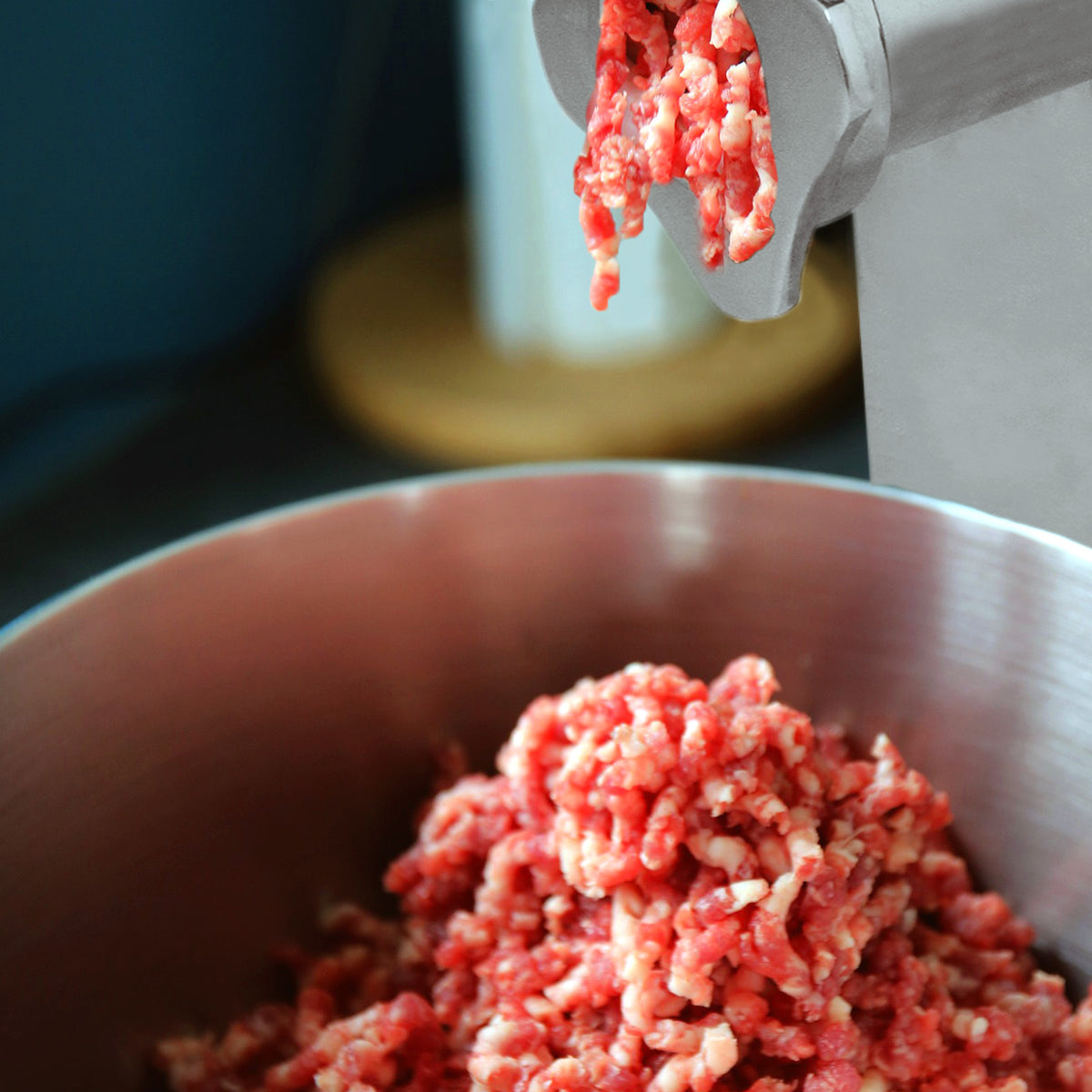 Red ground meat being extruded from the stainless steel KuKoo Commercial Meat Grinder into a large metal bowl, showcasing texture and freshness