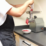 Stainless steel KuKoo commercial meat grinder with ground beef being processed into a white bowl on a black countertop