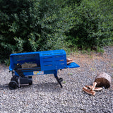 Bright blue electric log splitter on gravel, with split logs nearby and greenery in the background, showcasing its sturdy design and functionality