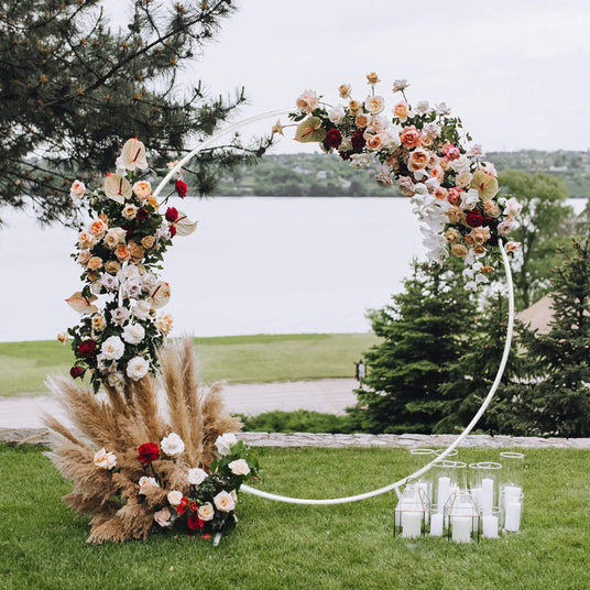 Elegant floral arch adorned with roses and greenery, surrounded by candles, set against a serene lakeside backdrop
