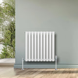 White oval single column radiator with chrome valves, 600mm x 600mm, mounted on a wall in a bright, modern room with wooden flooring