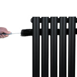 Sleek black oval single column radiator with smooth vertical bars, being cleaned with a brush for maintenance and upkeep