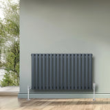 Oval single column radiator in anthracite grey, 600mm x 1020mm, featuring sleek vertical bars and chrome valves, set against a light green wall
