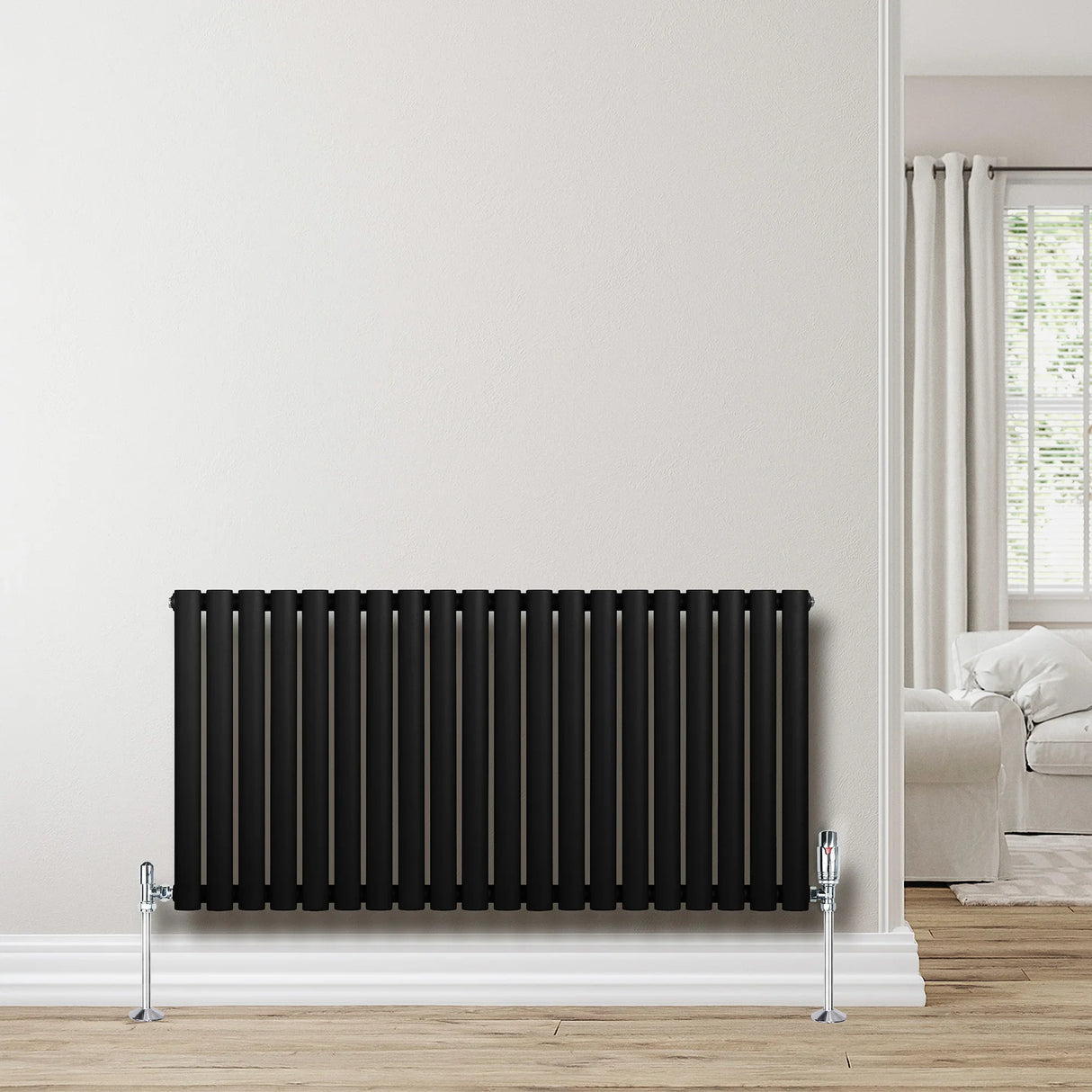 Sleek black oval single column radiator with polished valves, set against a light wall in a modern living space with wooden flooring