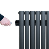 Anthracite grey oval single column radiator with a hand cleaning it, showcasing its sleek design and smooth texture