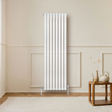 Sleek white oval single column radiator, 1600mm x 480mm, mounted on a wall in a cozy room with wooden flooring and decor