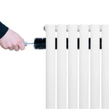 White oval single column radiator being cleaned with a brush, showcasing its smooth finish and sleek design for modern interiors