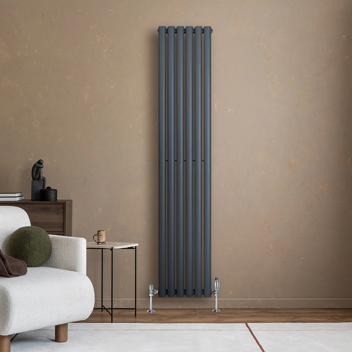 Sleek anthracite grey oval single column radiator standing against a textured beige wall, complemented by modern furniture and decor