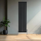 Flat black single column radiator with sleek vertical lines, paired with chrome valves, set against a minimalist interior backdrop