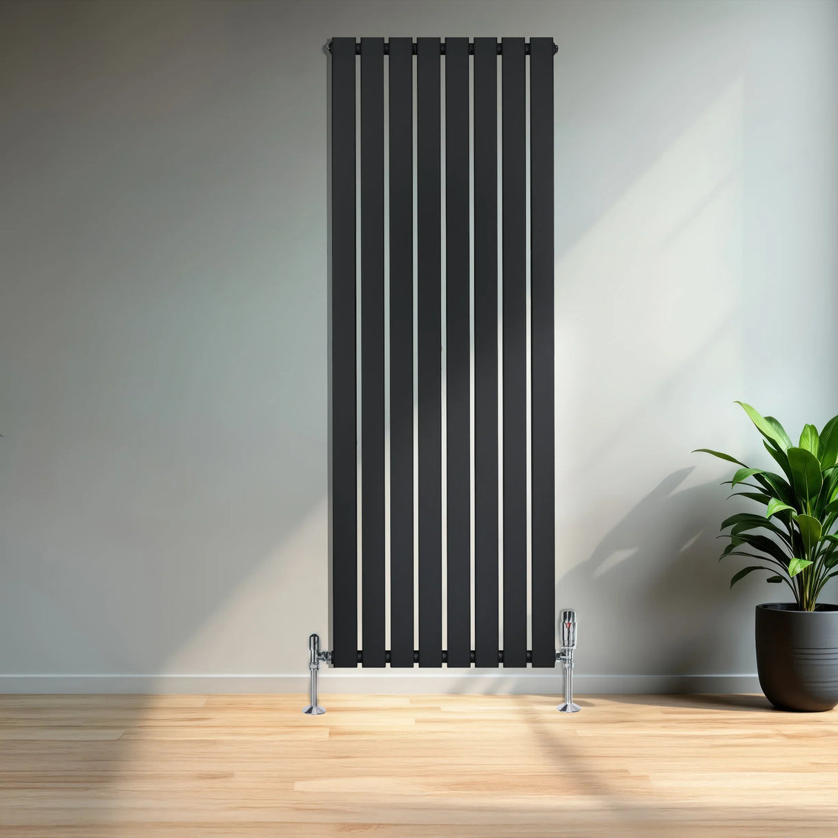 Flat black single column radiator with vertical slats, standing on the floor beside a potted plant in a modern room setting