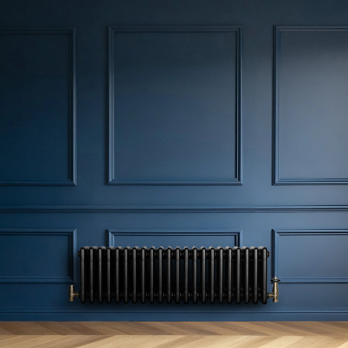 Traditional black 4 column radiator with brass valves, mounted on a deep blue wall, complementing a herringbone wood floor