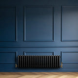 Traditional black 4 column radiator with brass valves, mounted on a deep blue wall, complementing a herringbone wood floor