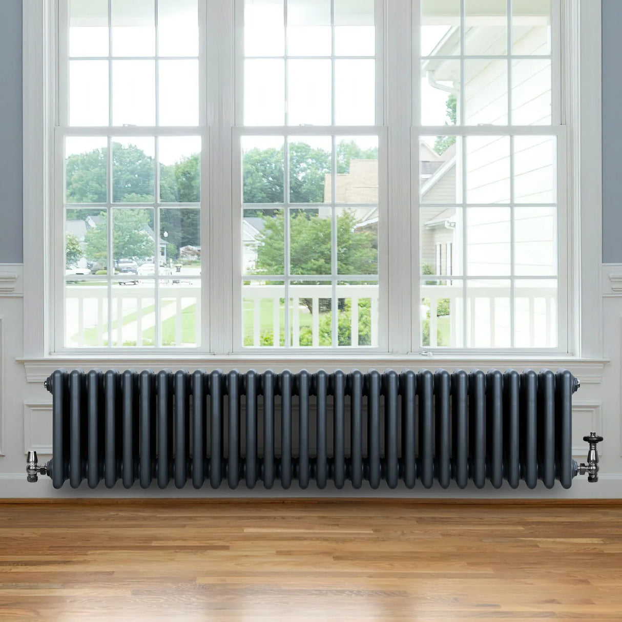 Traditional anthracite grey 4 column radiator with valves, showcasing a sleek design against a bright window and wooden floor