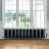 Traditional anthracite grey 4 column radiator with valves, showcasing a sleek design against a bright window and wooden floor