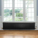 Traditional black 4 column radiator with brass valves, showcasing a sleek design against a bright window backdrop and wooden floor